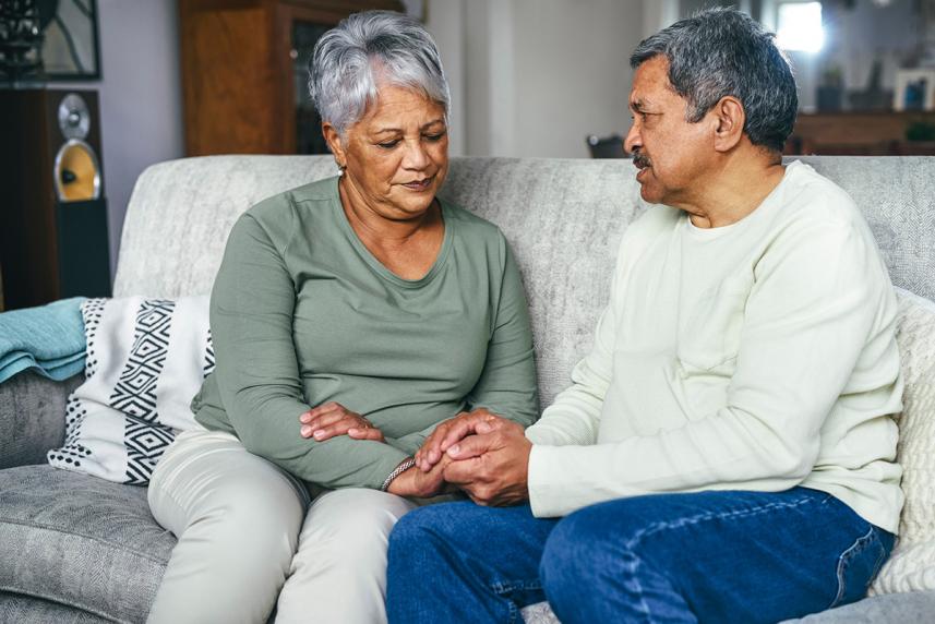 Senior couple holding hands while sitting on a couch