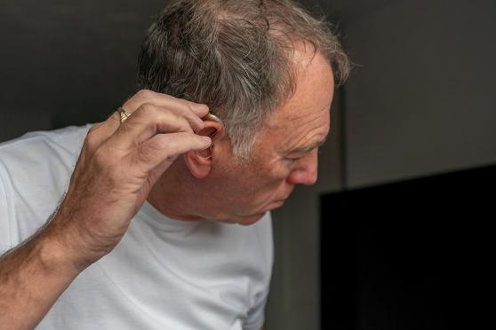 A man touching the hearing aid on his ear